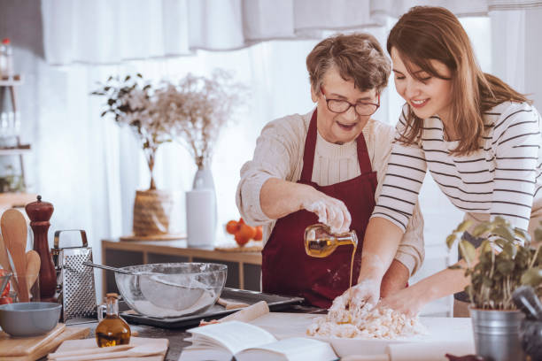 Grandmother adding oil to dough Grandmother helping her granddaughter make dough by adding olive oil easter cake photos stock pictures, royalty-free photos & images