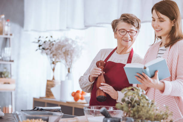 Young woman holding cookbook and grandmother holding pepper mill