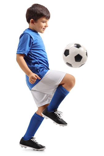 Full length profile shot of a little footballer juggling a football isolated on white background
