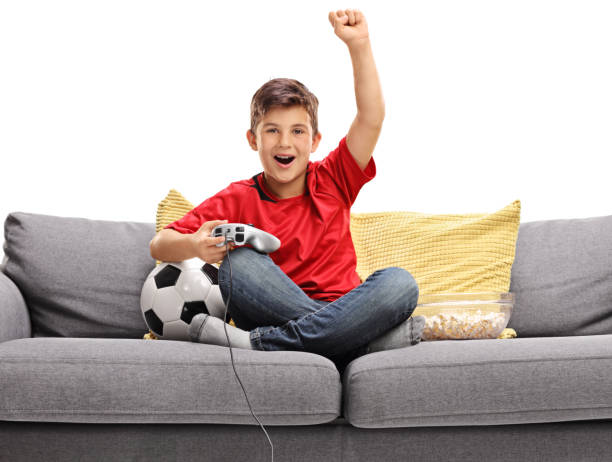 Joyful little boy sitting on a sofa and playing a soccer video game Joyful little boy sitting on a sofa and playing a soccer video game isolated on white background popcorn snack bowl isolated stock pictures, royalty-free photos & images