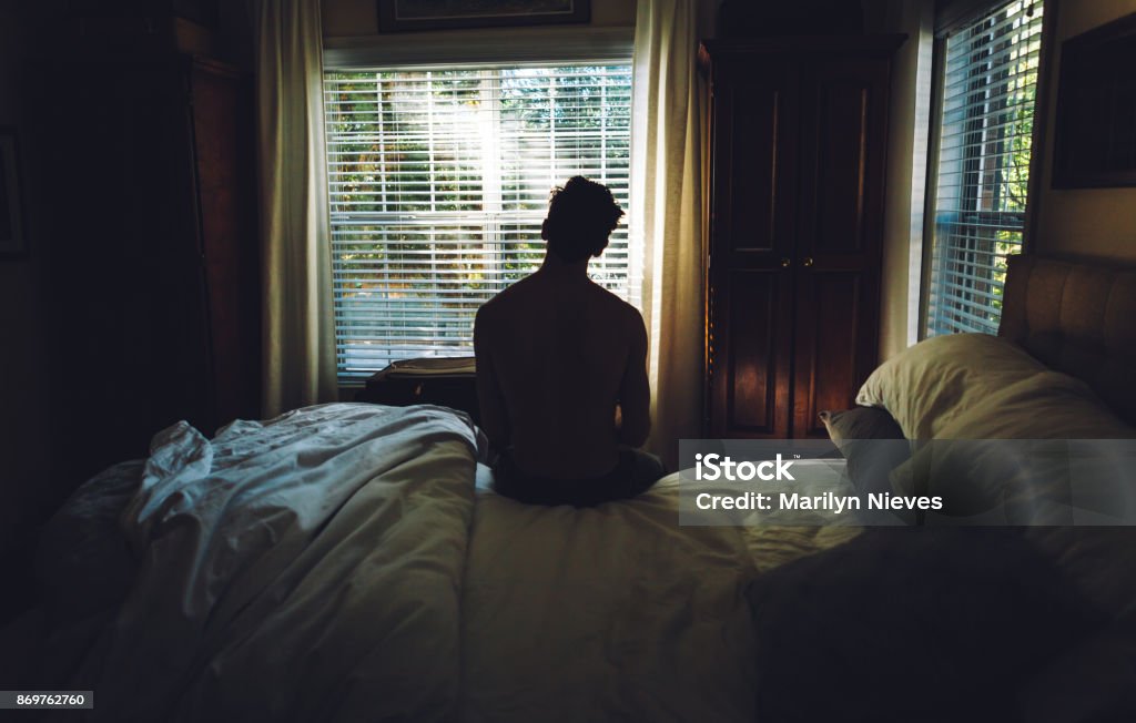 tired man waking up in the morning Man sitting up in bed in the early morning. Waking up Stock Photo
