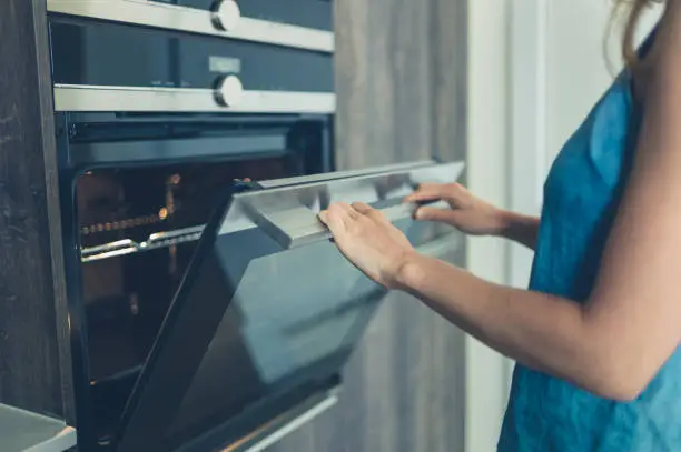 A young woman is opening the oven in her modern kitchen