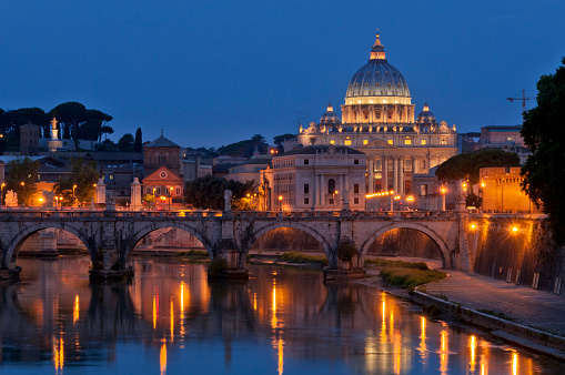 Vatican city and an illuminated dome of Basilica di San Pietro at night, with reflection on the River Tiber.
