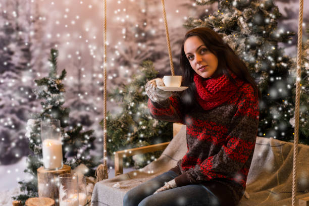 istock Young female sitting on a swing with a blanket under the flashlights and offering a cup of coffee 869773372