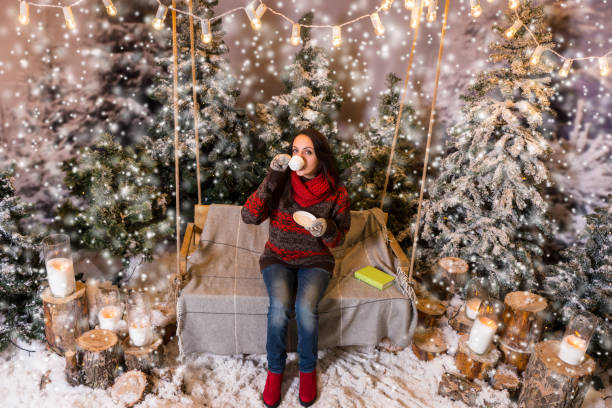 istock Young female sitting on a swing with a blanket under the flashlights and drinkig a cup of coffee in a snow-covered park 869774030