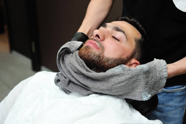 Barber preparing man face for shaving with hot towel on face in barber shop.