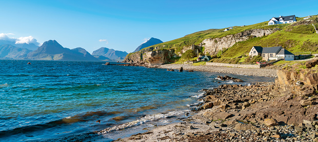 Landscape stock photograph of rocky coastline and the Cuillin Mountains visible in the distance in Elgol, Isle of Skye, Scotland, United Kingdom.