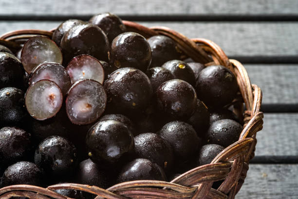 jabuticabas, auch bekannt als brasilianische beere oder brasilianischen grapetree (plinia cauliflora) früchte auf einem hölzernen rebe-korb, mit einem schwarzen hintergrund aus holz - berry vine stock-fotos und bilder