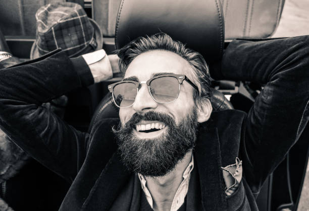 Fashion portrait of young bearded man ready for road trip - Cheerful hipster guy sitting in car looking the sky - Black and white editing - Soft focus on beard - Warm vintage retro filter Fashion portrait of young bearded man ready for road trip - Cheerful hipster guy sitting in car lokking the sky - Black and white editing - Soft focus on beard - Warm vintage retro filter black and white men facial hair beard stock pictures, royalty-free photos & images