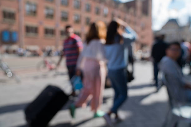 Busy street background scene in Amsterdam on Damrak people moving about defocused and blurred in motion two unrecognizable women one pulling black suitcase