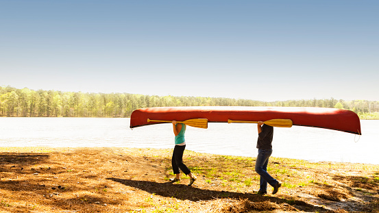 Couple carrying a red canoe near a lake.