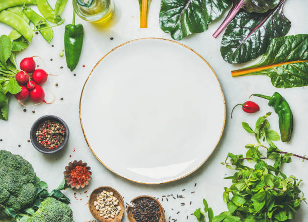 fresh greens, vegetables and grains with white plate in center - vegan food still life horizontal image imagens e fotografias de stock
