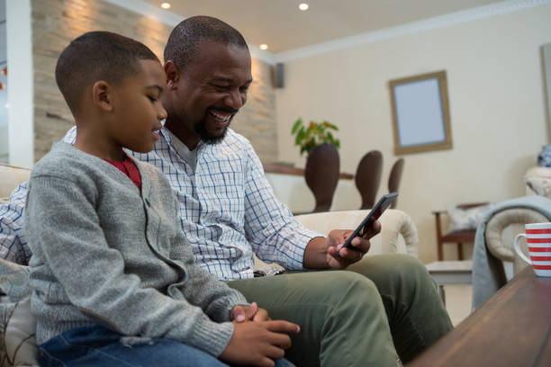 istock Father and son using mobile phone on sofa in living room 869830060