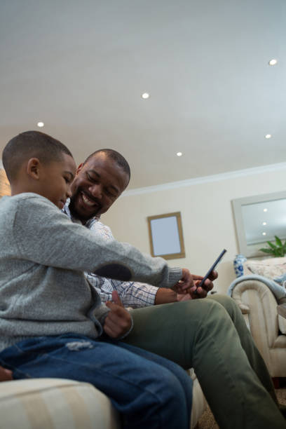 istock Father and son using mobile phone on sofa in living room 869830394