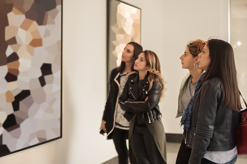 Four girl friends looking at modern painting in art gallery. Abstract painting