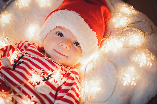 Cute baby boy wearing reindeer costume, Santa hat and holding Christmas lights