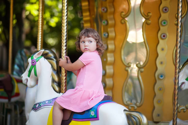 Cute little girl at the theme park, riding retro merry-go-round carousel.