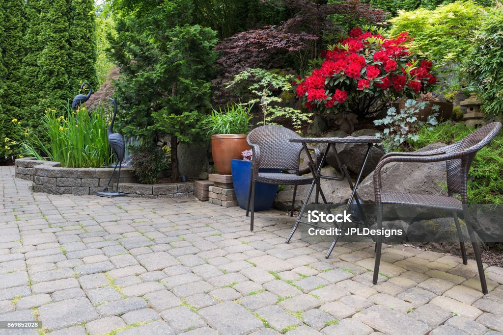 Garden backyard with lush plants landscaping pond water fountain and stone paver patio hardscape with wicker bistro furniture chair and table set Patio Stock Photo