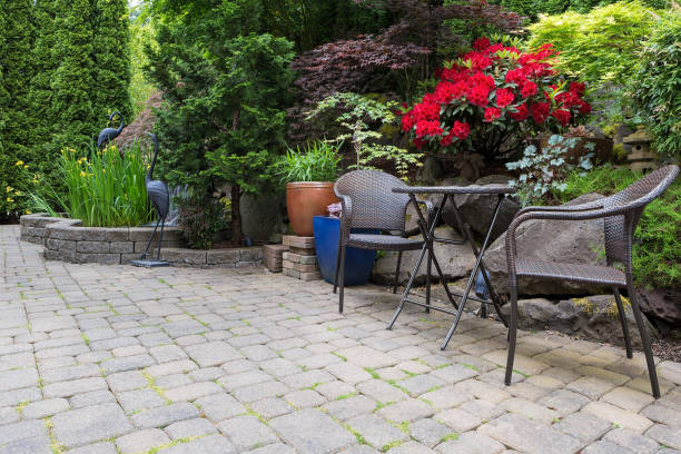 Garden backyard with lush plants landscaping pond water fountain and stone paver patio hardscape with wicker bistro furniture chair and table set Garden backyard with lush plants landscaping pond water fountain and stone paver patio hardscape with wicker bistro furniture chair and table set hardscape photos stock pictures, royalty-free photos & images
