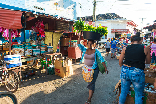 Street Market in the morning in Granada, in front view local women has basket with vegetable on her head, stalls with eggs and other food on sale. Nicaragua