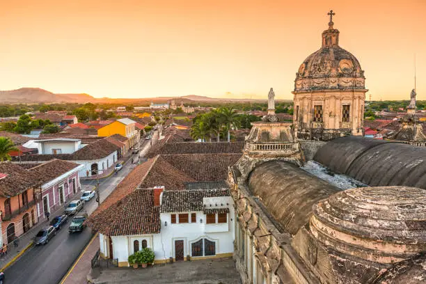 Skyline of old city Granada in Nicaragua at sunset. View from bell tower on colorful houses and street with some cars and unrecognizable people.