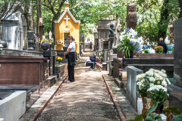 A mother and her son honor their loved ones at a serene cemetery with flickering candles and beautiful flowers