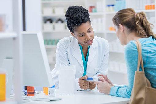 Caucasian female pharmacy customer discusses an over the counter medication with confident female pharmacist.