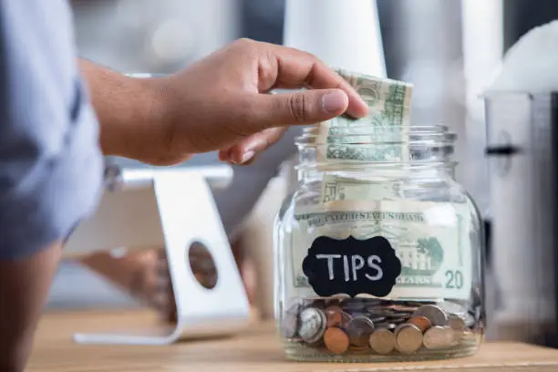 Photo of Coffee shop customer places cash in a tip jar