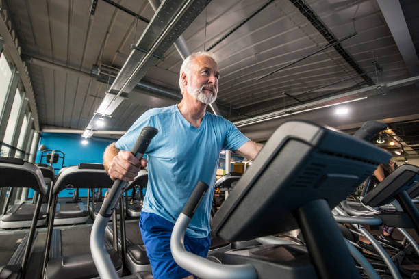 homme senior sain gardant rentre dans la salle de gym sur un cross trainer - cross trainer photos et images de collection