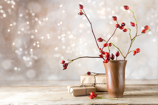 small gift parcels and rosehip branches on a rustic wooden table against a vintage wall with blurred bokeh lights, autumn or christmas decoration with copy space, selected focus