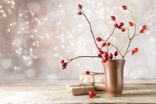 small gift parcels and rosehip branches on a rustic wooden table against a vintage wall with blurred bokeh lights, autumn or christmas decoration with copy space small gift parcels and rosehip branches on a rustic wooden table against a vintage wall with blurred bokeh lights, autumn or christmas decoration with copy space, selected focus winter still life stock pictures, royalty-free photos & images