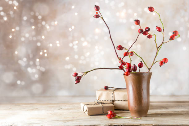 small gift parcels and rosehip branches on a rustic wooden table against a vintage wall with blurred bokeh lights, autumn or christmas decoration with copy space - nature herb flower arrangement cut flowers imagens e fotografias de stock