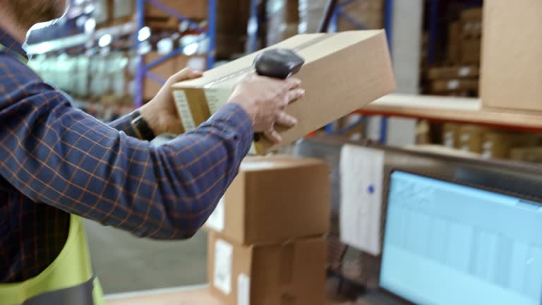 Male warehouse employee scanning packages on a desk in the warehouse with a handheld scanner