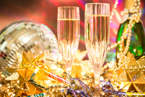 New Year's Eve celebration party with champagne, glasses, disco ball, decorations including: beads, lights, party horn blowers, and streamers.  Home party or nightclub setting.