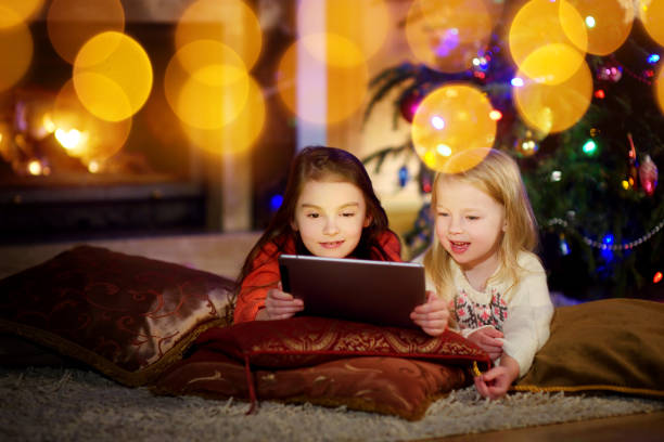 istock Two cute little sisters using a tablet pc by a fireplace on Christmas evening 869943676