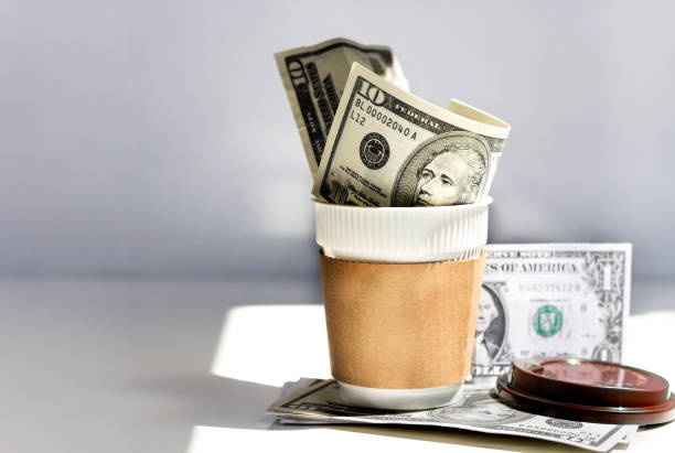 Dollar banknotes with a cup made of plastic on the table.