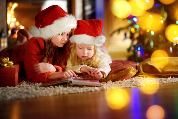 istock Two cute little sisters reading a story book together under a Christmas tree 869949978