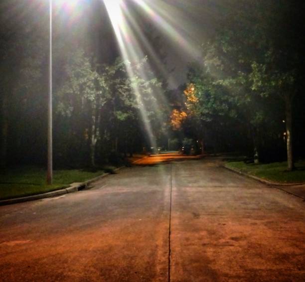Beams of light from a tall streetlamp illuminate a dark suburban street in Clear Lake City, Houston, Texas.