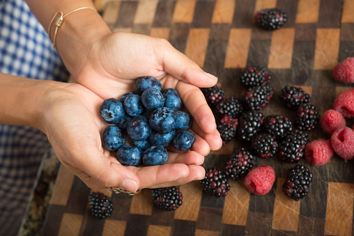 Woman's hands holding a handful of fresh ripe in-season blackberries against a white background. Blackberries are rich in vitamins and nutrients.