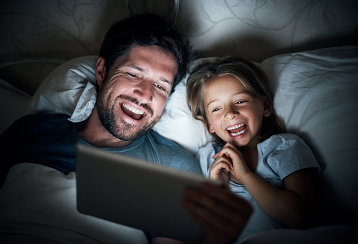 Shot of an adorable little girl and her father using a digital tablet together at night in bed