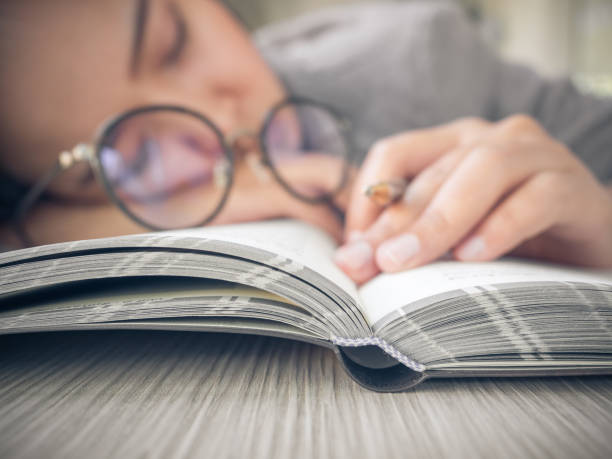 étudiante/femme d’affaires somnolent s’endormir sur un livre avec des lunettes au cours de l’étude - pillow wake up yawning sleeping photos et images de collection