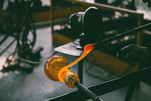The Details and Close-up of a worker shaping liquid glass at a glass factory.