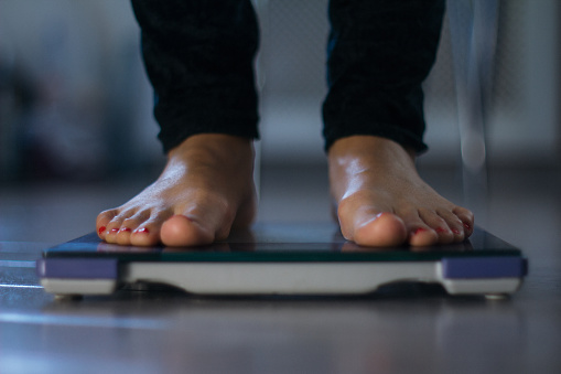 Female measuring weight on health scale close-up. Woman legs approaching to weighing digital instrument