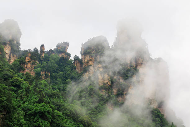 istock Huge Rock Mountains Surrounded by Green Trees and White Mist Clouds. Epic Mountain Landscape 870003892