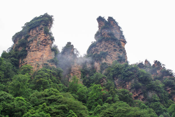 istock Beautiful Rock Mountains with Green Trees Surrounded by White Mist Clouds. Green Mountain Landscape 870004196