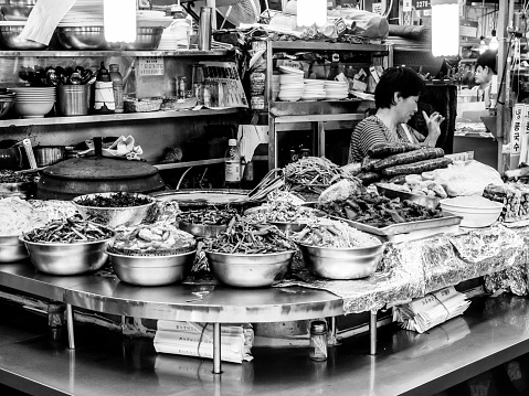 Seoul, South Korea - June 21, 2017: Woman vendor waiting customers at Gwangjang Market in Seoul. Gwangjang Market Eatry Alley  is the  market with a long history beginning in 1905. One of the most popular street food  place where you can buy gimbap, teokbokki, bibimbap, kimchi.