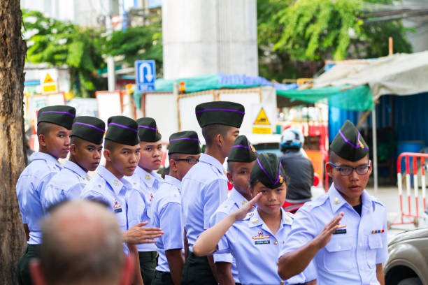 Capture of a group of thai army cadets in uniforms salutating while standing on sidewalk of Phahonyothin Road in Bangkok. They are salutating to an officer passing by.