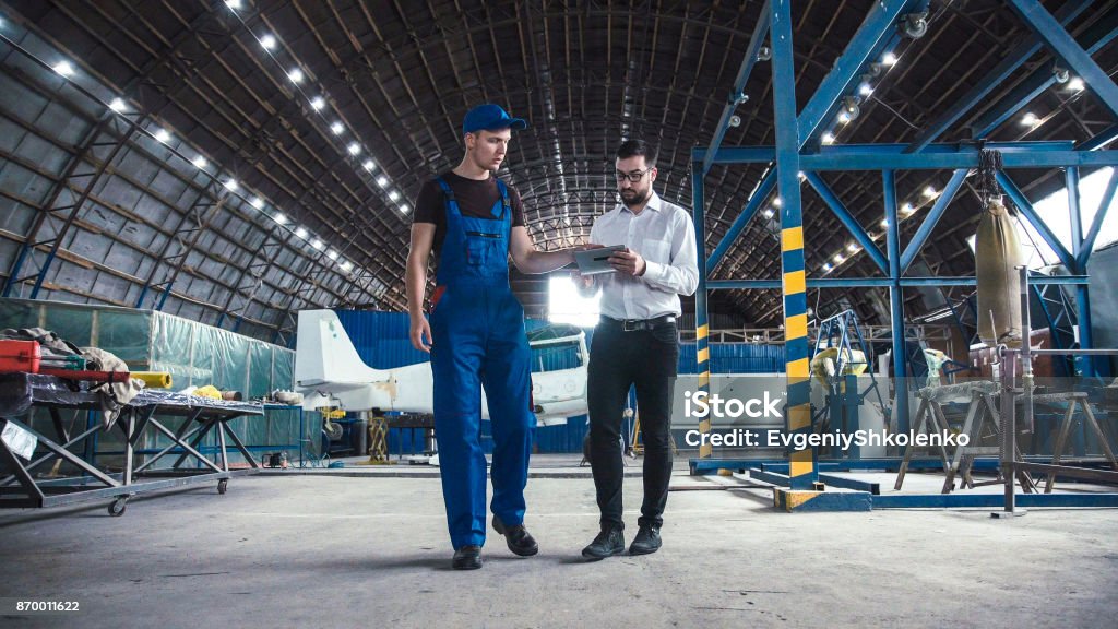 Mechanic and flight engineer having a discussion Mechanic and flight engineer having a discussion together as they stand in aircraft in a hangar. Airplane Stock Photo