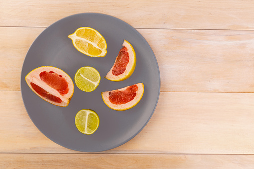 Sliced lemons, grapefruit and lime on a gray plate that is on a beige table. View from above