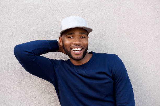 istock attractive man standing with hand behind head and smiling by wall 870026388